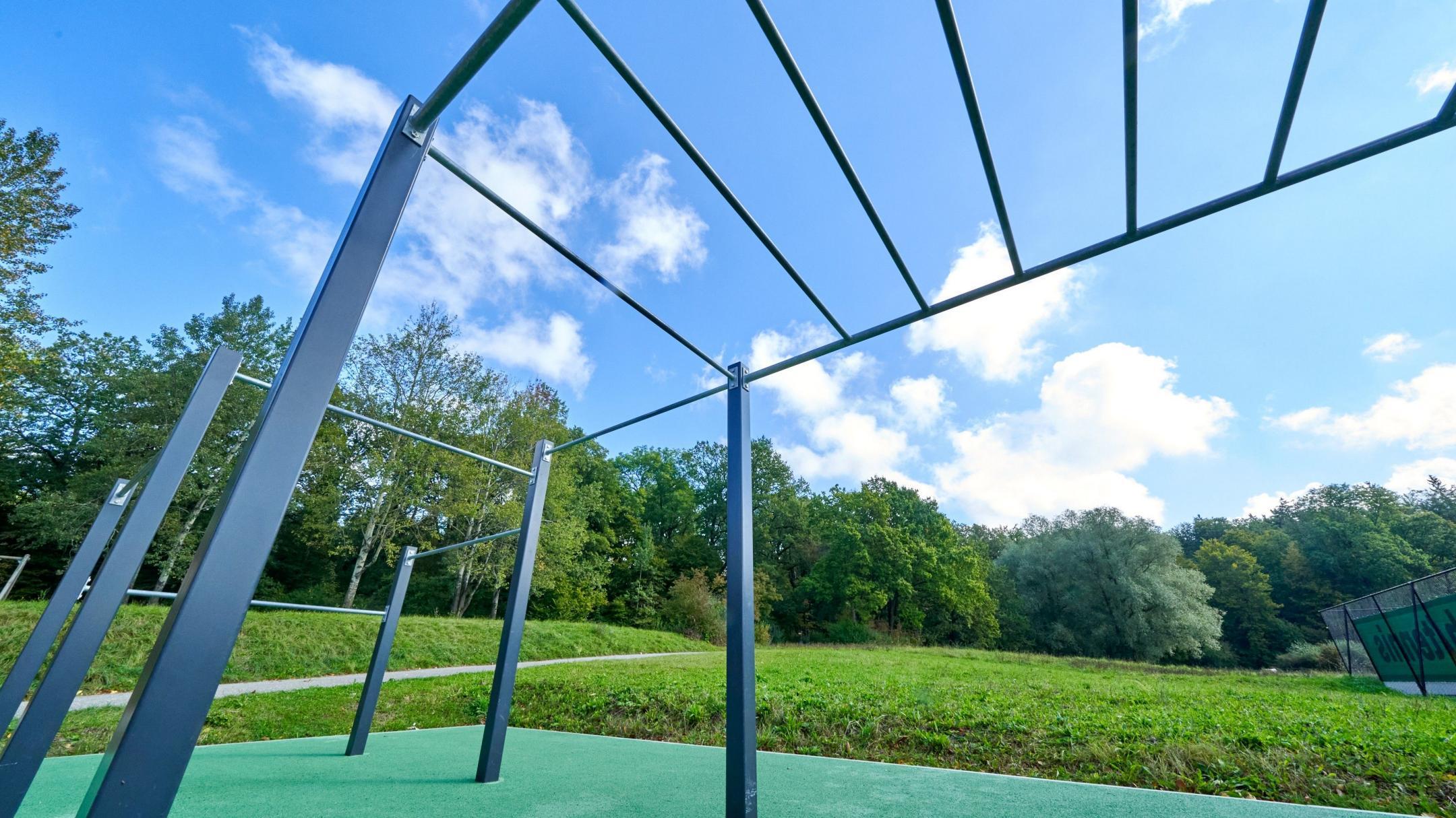 Ein Outdoor-Trainingsgerät in einem Park mit grüner Wiese und Bäumen unter blauem Himmel.