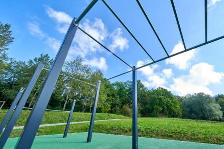 Ein Outdoor-Trainingsgerät in einem Park mit grüner Wiese und Bäumen unter blauem Himmel.