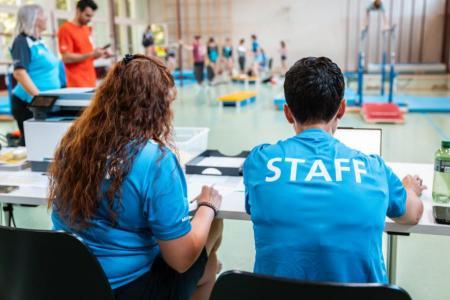 Zwei Personen sitzen an einem Tisch in einem blauen Shirt mit Schriftzug «Staff»