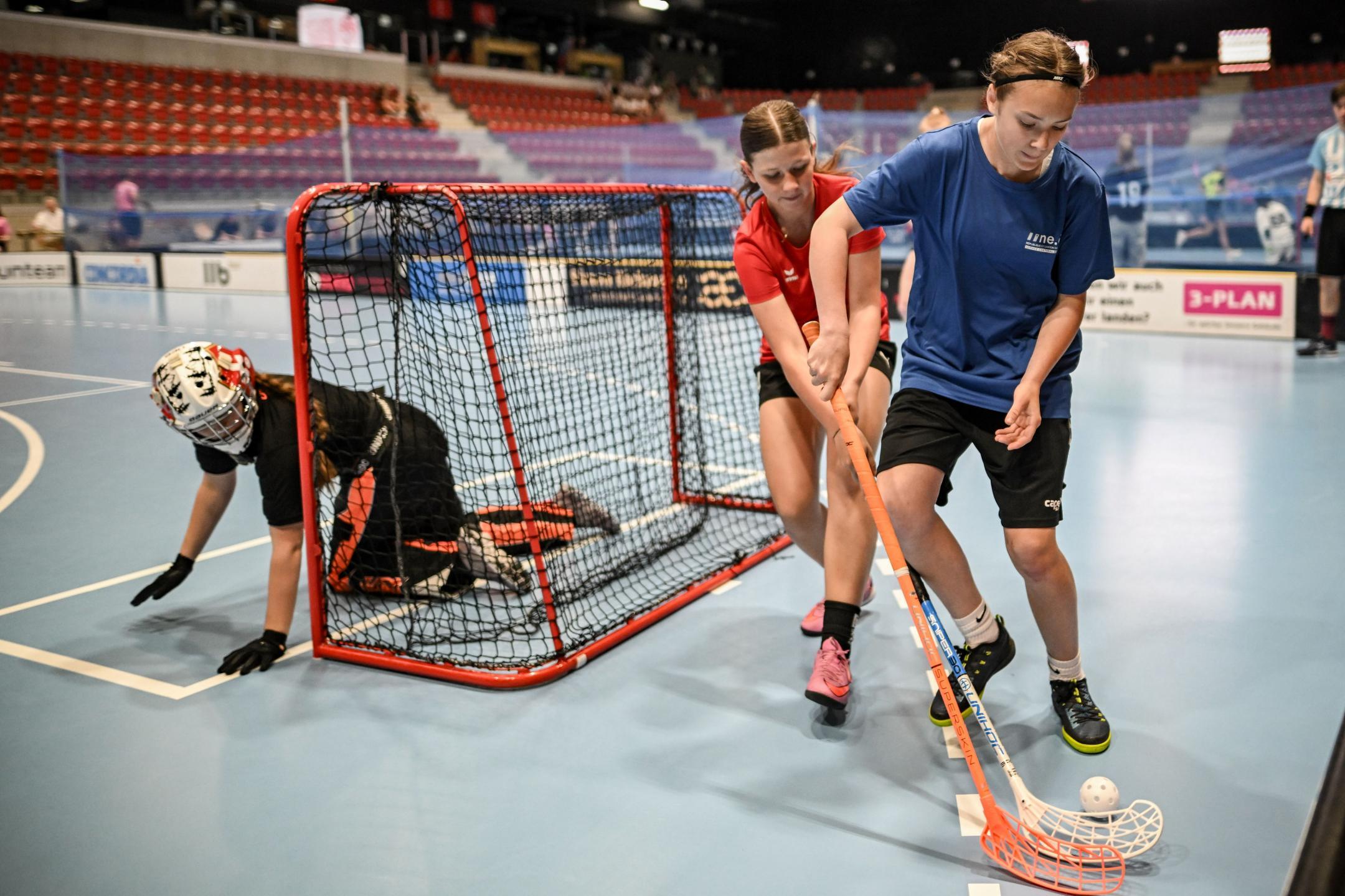 Drei Mädchen spielen Unihockey in einer Halle.