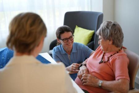 Eine Pflegefachperson spricht mit einer älteren Frau in einem Aufenthaltsraum.