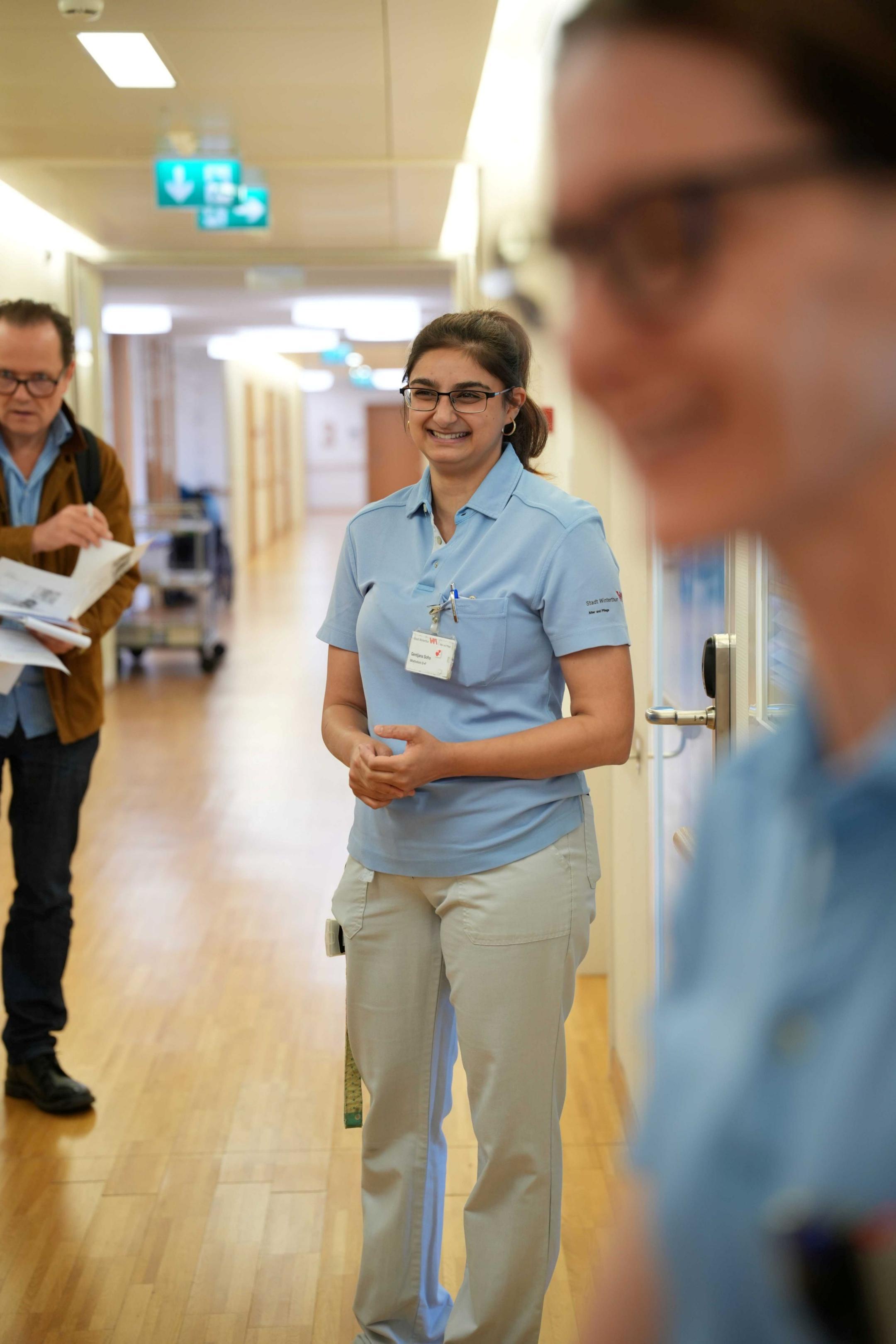 Eine Pflegefachperson steht lächelnd auf dem Flur.