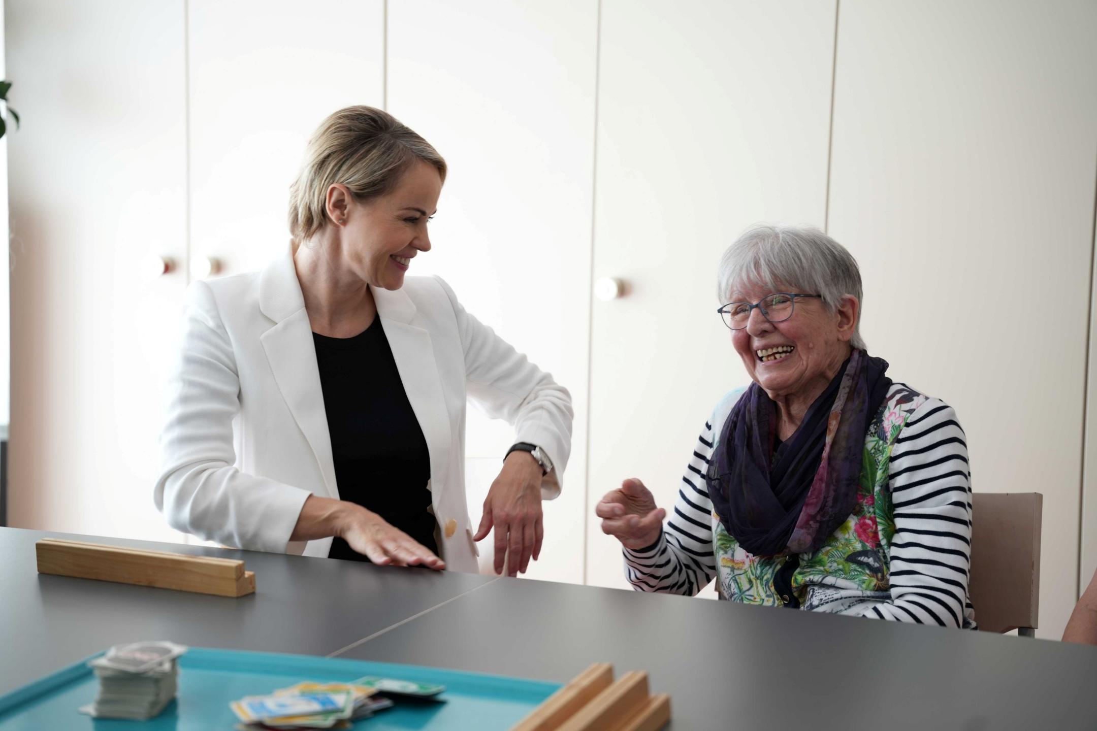Gesundheitsdirektorin Natalie Rickli spricht lächelnd mit einer älteren Frau an einem Tisch.