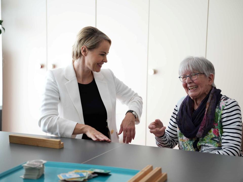 Gesundheitsdirektorin Natalie Rickli spricht lächelnd mit einer älteren Frau an einem Tisch.