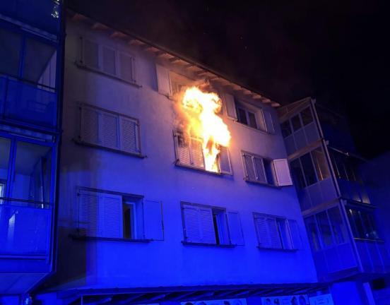 Ein Mehrfamilienhaus bei dem aus einem Fenster Flammen schlagen