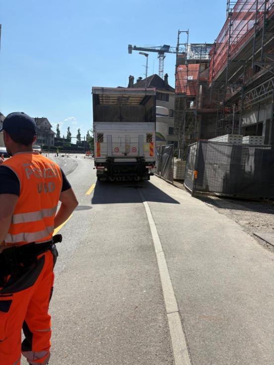 Ein am Strassenrand parkierte Lastwagen, rechts davor ein Polizist in oranger Kleidung.