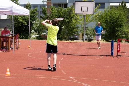 Ein Knabe und ein Mann machen Tennis-Spielformen auf einem roten Platz.