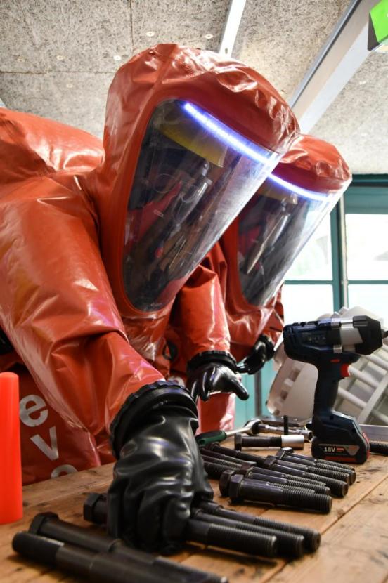 Männer in orangen Schutzanzügen reichen die bereitliegenden Schrauben 