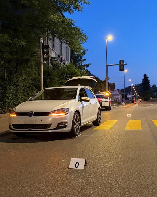 weisses Unfallfahrzeug steht auf der Strasse und halb auf einem Fussgängerstreifen bei morgentlicher Dämmerung. Im Hintergrund ein Polizeiauto und Verkehrsdienste sowie Signalisationsmaterial