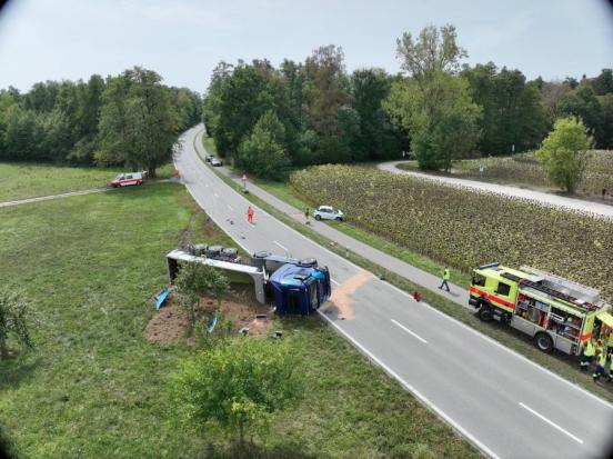 Ein Lastwagen liegt auf der Seite in der Wiese. Auf der anderen Strassenseite steht ein weisser Kleinwagen in der Wiese.