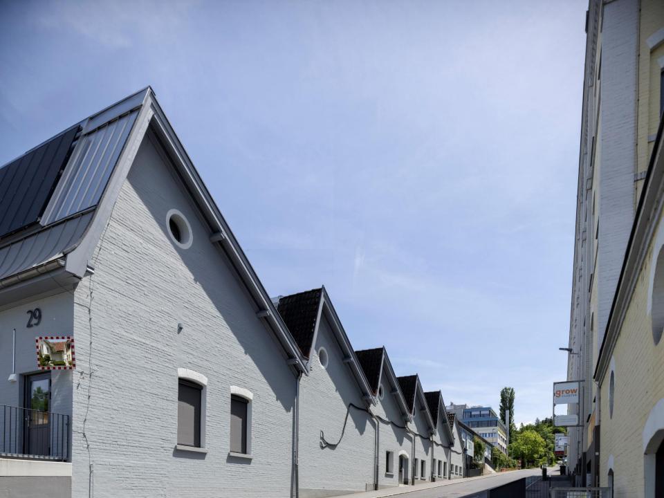 Reihe von grauen Lagerhallen mit gezackten Dächern und runden Fenstern, an einer Strasse. Die Nummer «29» ist an der ersten Halle zu sehen.