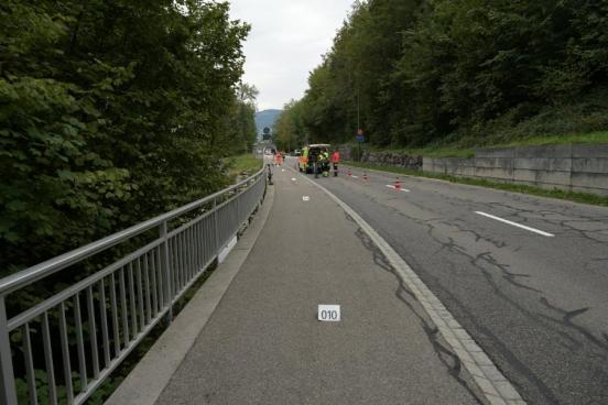 Eine teilweise abgesperrte Strasse mit einem Einsatzfahrzeug der Feuerwehr und weissen Distanzmarkierungen am Boden