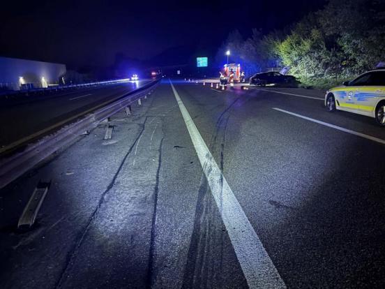 Eine Unfallstelle bei Nacht auf einer Autobahn mit dem Unfallfahrzeug, einem Polizeiauto und einem Rettungswagen.