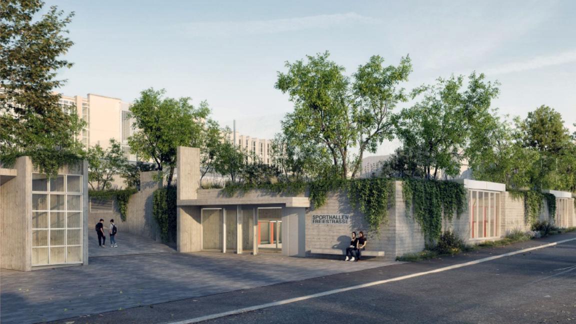 Aussenaufnahme eines modernen Sichtbetongebäudes mit der Aufschrift «SPORTHALLEN FREIESTRASSE» an der Fassade. Das Bauwerk ist mit Kletterpflanzen und Bäumen auf dem Dach begrünt. Im Vordergrund verläuft eine Strasse vor einem Vorplatz, auf dem zwei Personen auf einer Bank sitzen und weitere Passanten zu sehen sind. Im Hintergrund zeichnet sich ein grösseres Schulgebäude ab.