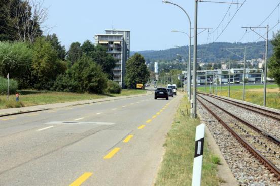 Blick entlang der zweispurigen Forchstrasse mit Blick auf die rechts verlaufenden Eisenbahngleise und Wohnhäuser im Hintergrund. 