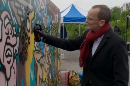 Martin Neukom steht vor einer Graffiti-Wand und vollendet mit einer Sprühdose das Graffiti.