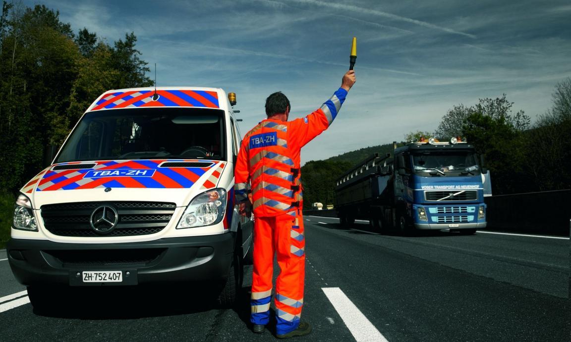 Ein TBA-Mitarbeiter beim Warnen des Verkehrs mit Kleidung und Fahrzeug in der Sicherheitssignaletik