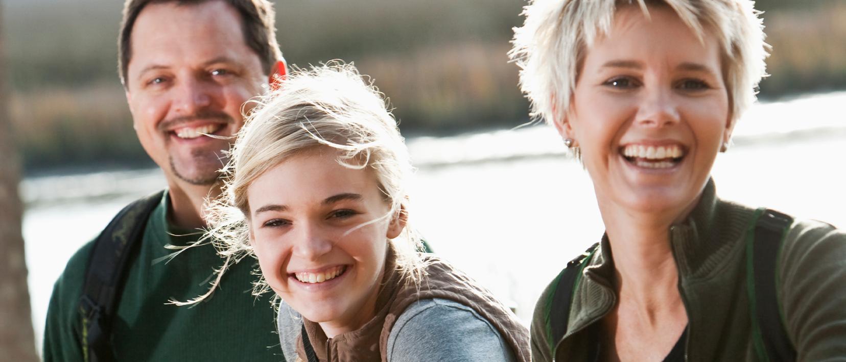 Das Bild zeigt eine Familie mit fröhlichem Gesichtsausdruck vor einem See.