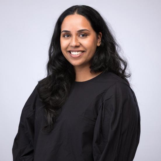 Gaaya schaut lächend in die Kamera. Sie träg ein schwarzes Oberteil und hat schwarze lange Haare.