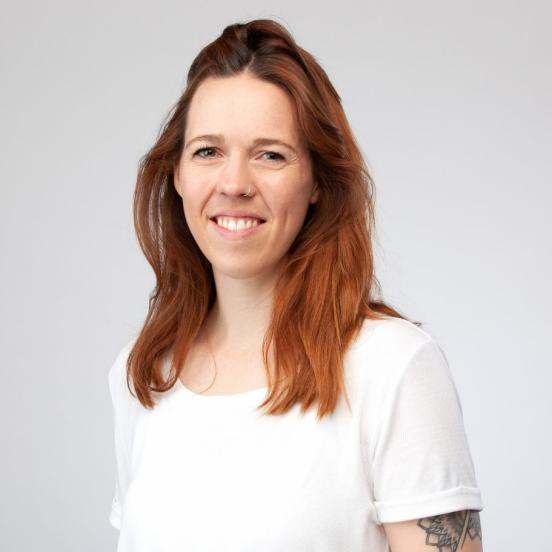 Maura Gysin hat rötliche Haare, trägt ein weisses T-Shirt. Es sind kleinere Tattoos am Arm zu sehen. Maura lächelt in die Kamera