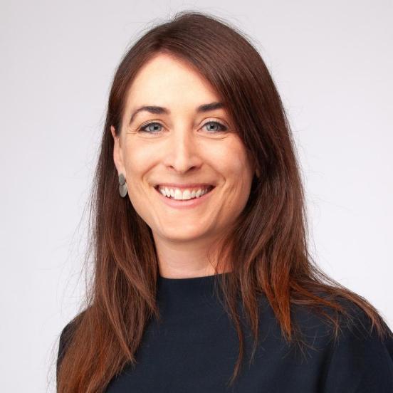 Susanne Nef hat lange braune Haare und helle Augen. Sie trägt ein schwarzes Oberteil und lacht in die Kamera