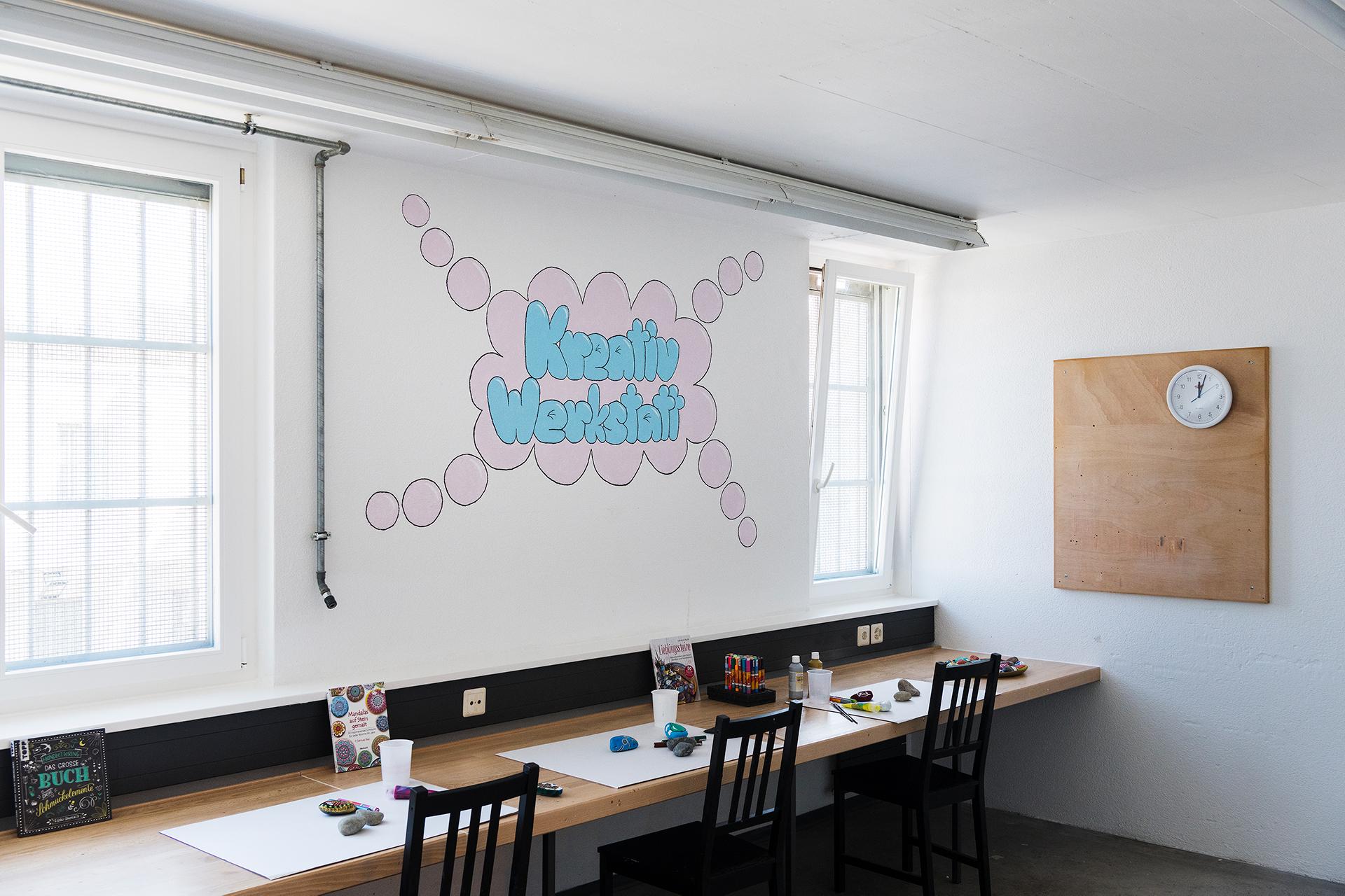 Malutensilien und bemalte Steine auf einem Tisch vor vergittertem Fenster