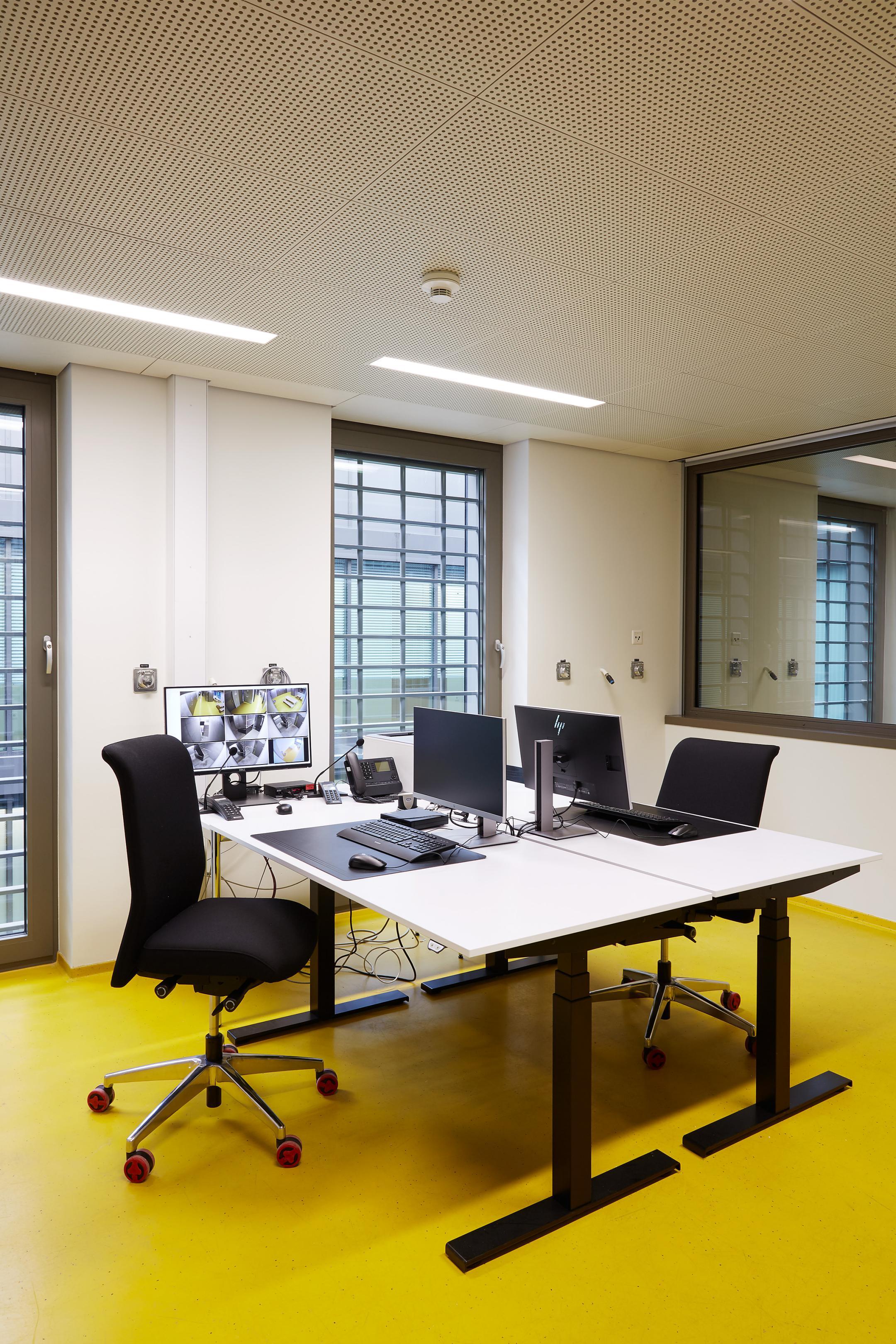 Raum mit vergitterten Fenstern und zwei Tischen mit Computern