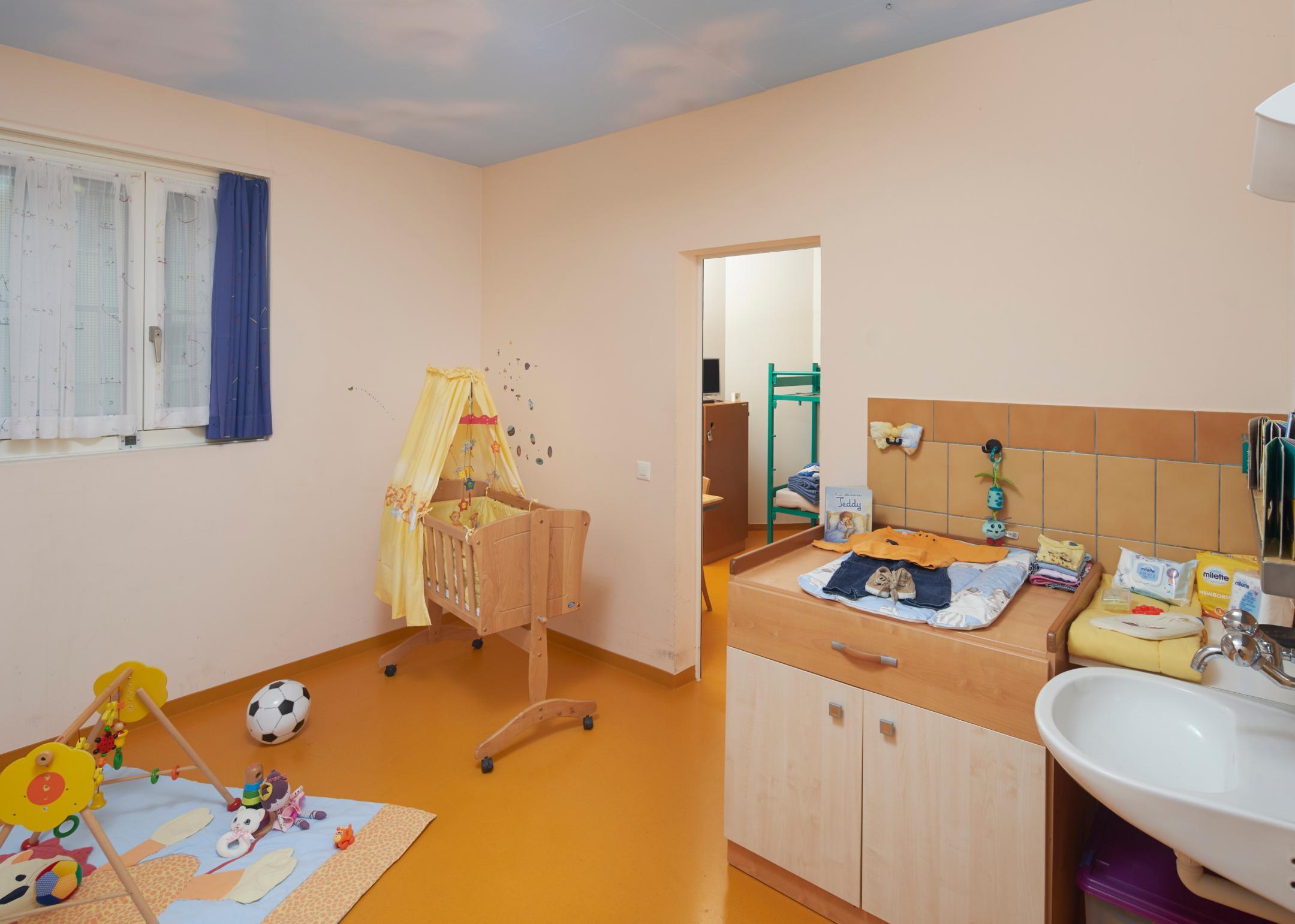 Raum mit Kinderkrippe, Spielzeug, Wickeltisch und Waschbecken.