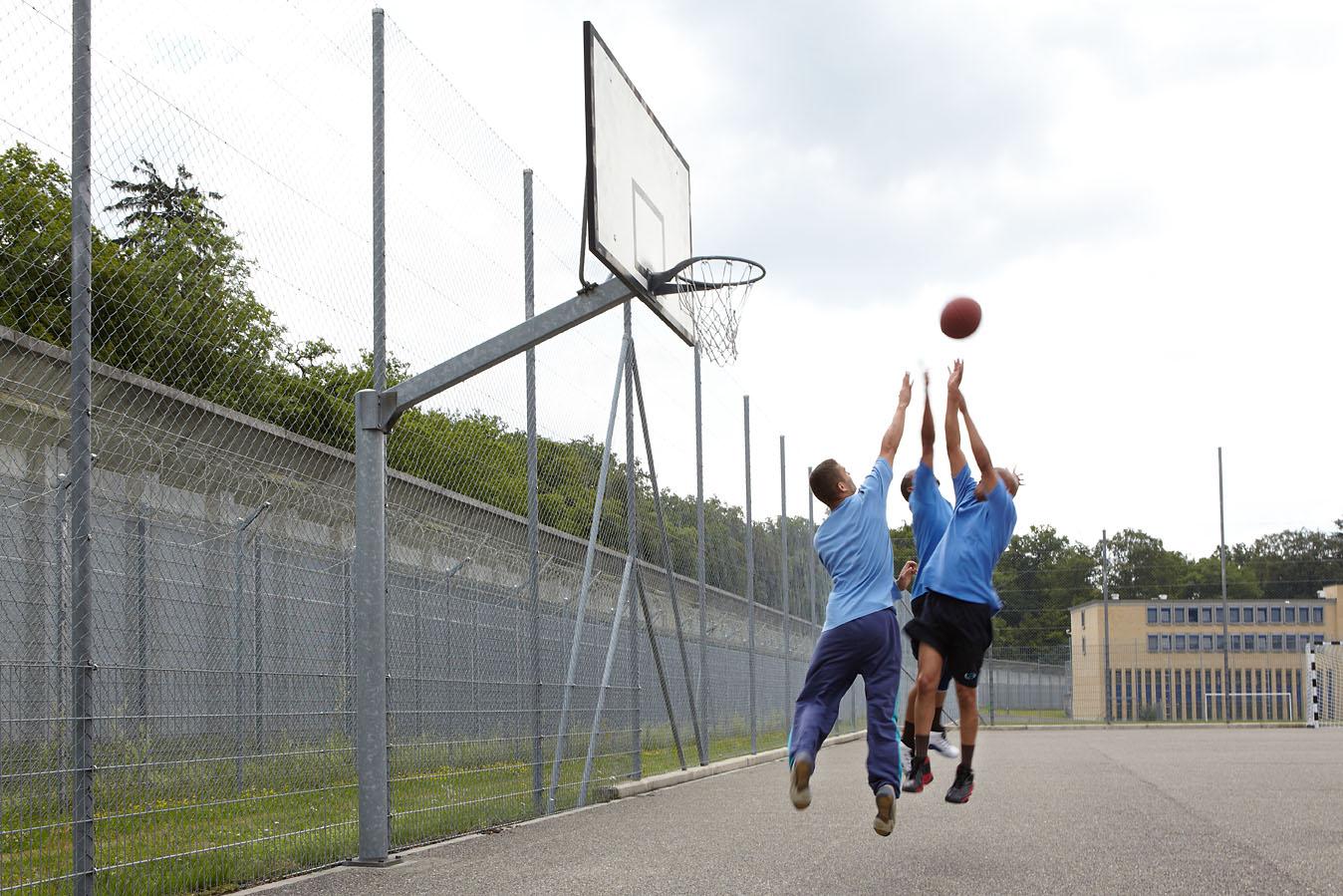 Drei Männer werfen Ball in Basketballkorb.