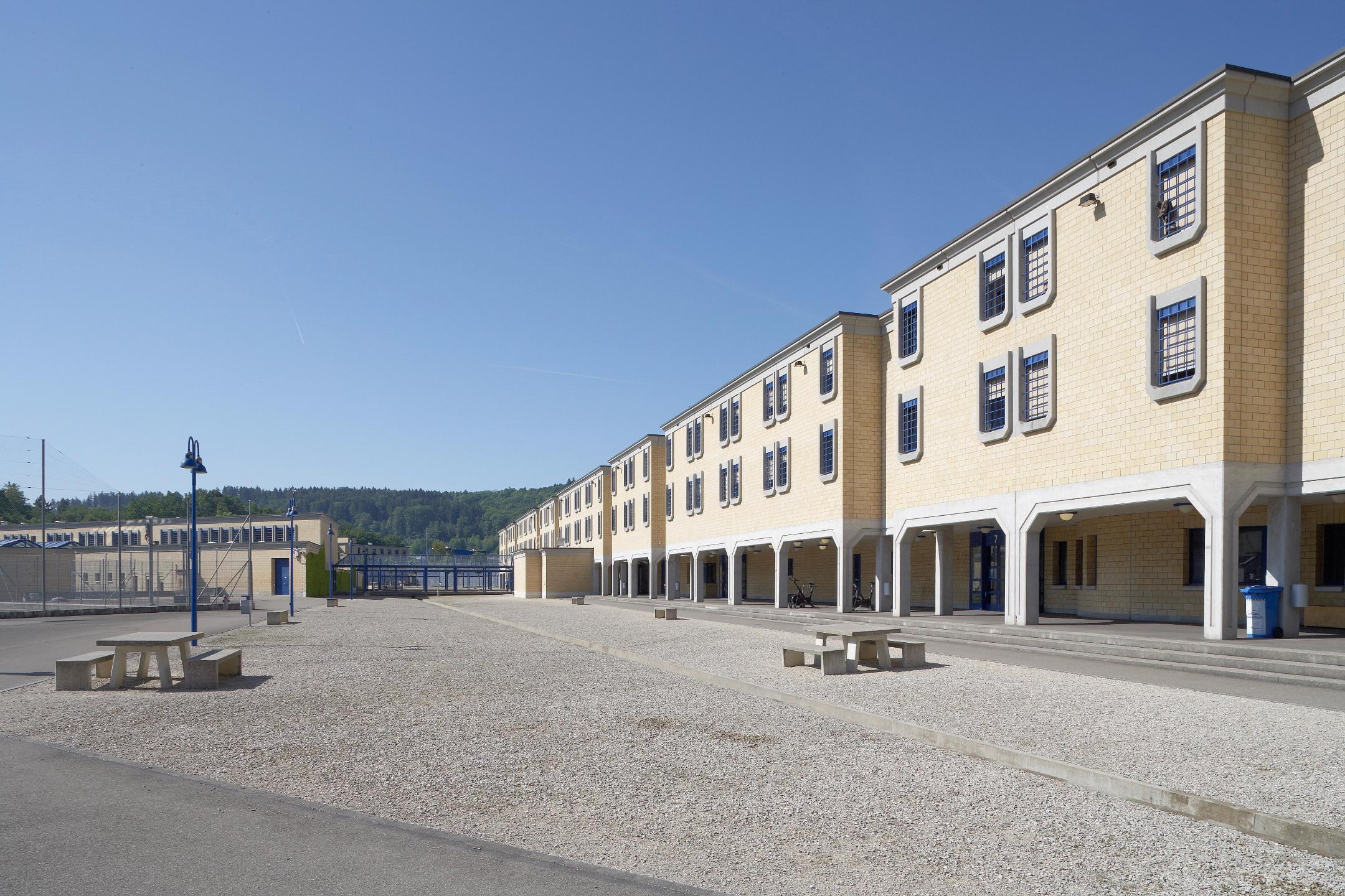 Umzäunter Hof mit Tischen und Bänken aus Beton.