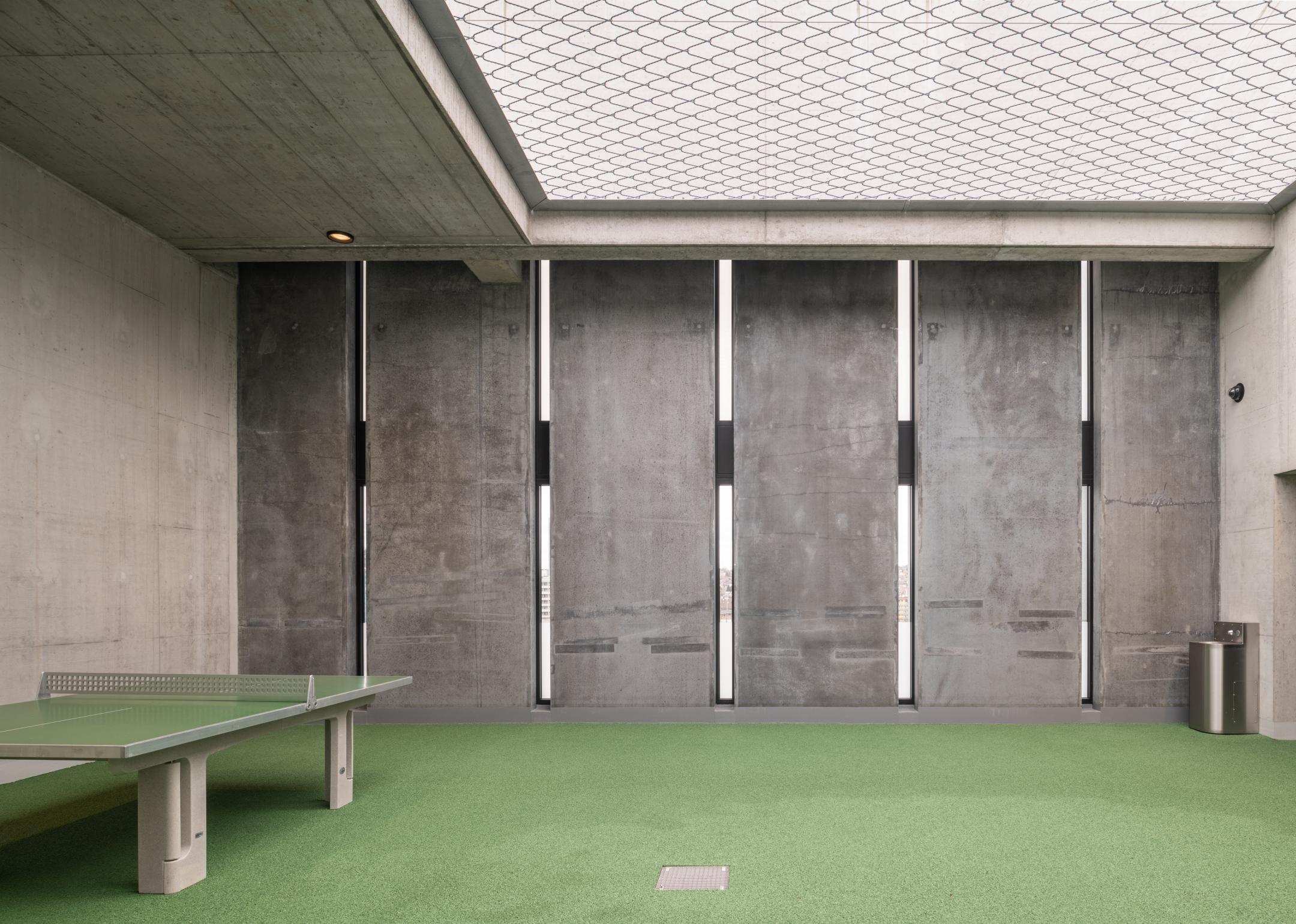 Ein Raum mit einem Gitternetz oben, einem grünen Boden und einer grünen Tischtennisplatte.