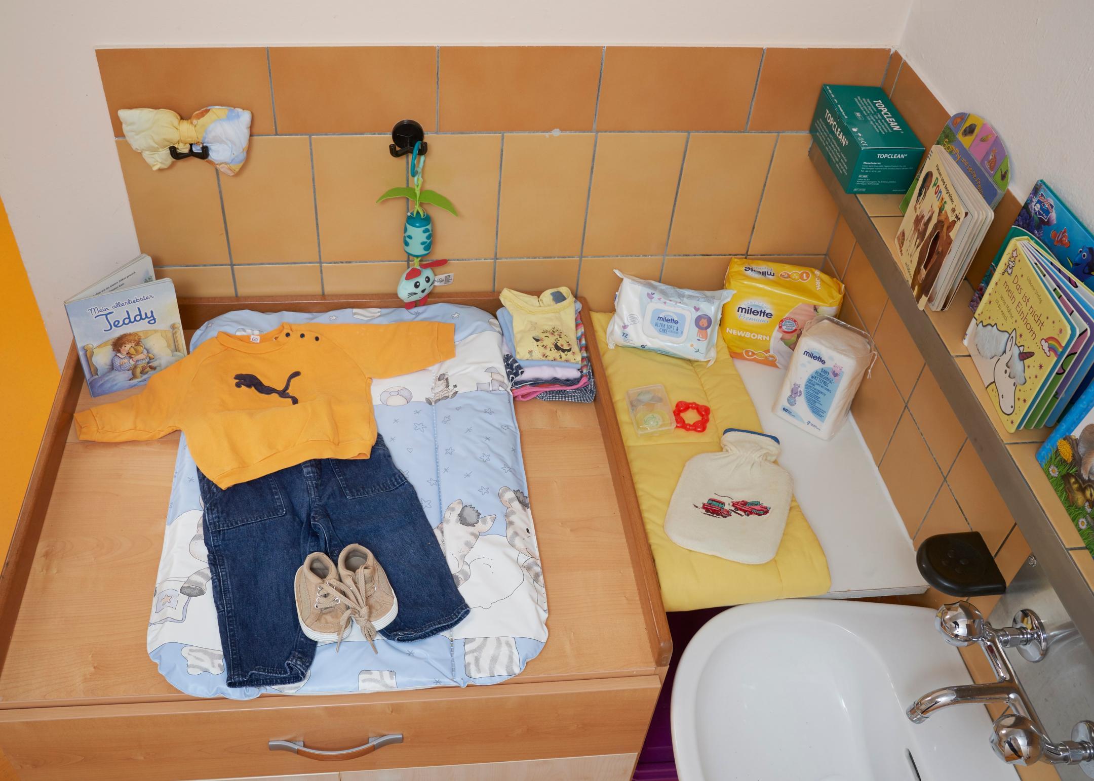 Wickeltisch mit Kinderkleidung, Kinderbüchern und Lavabo.