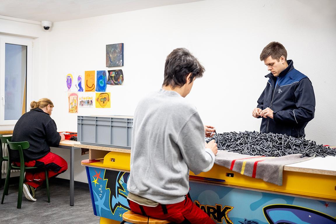 Zwei Inhaftierte und ein Aufseher sortieren Schrauben.