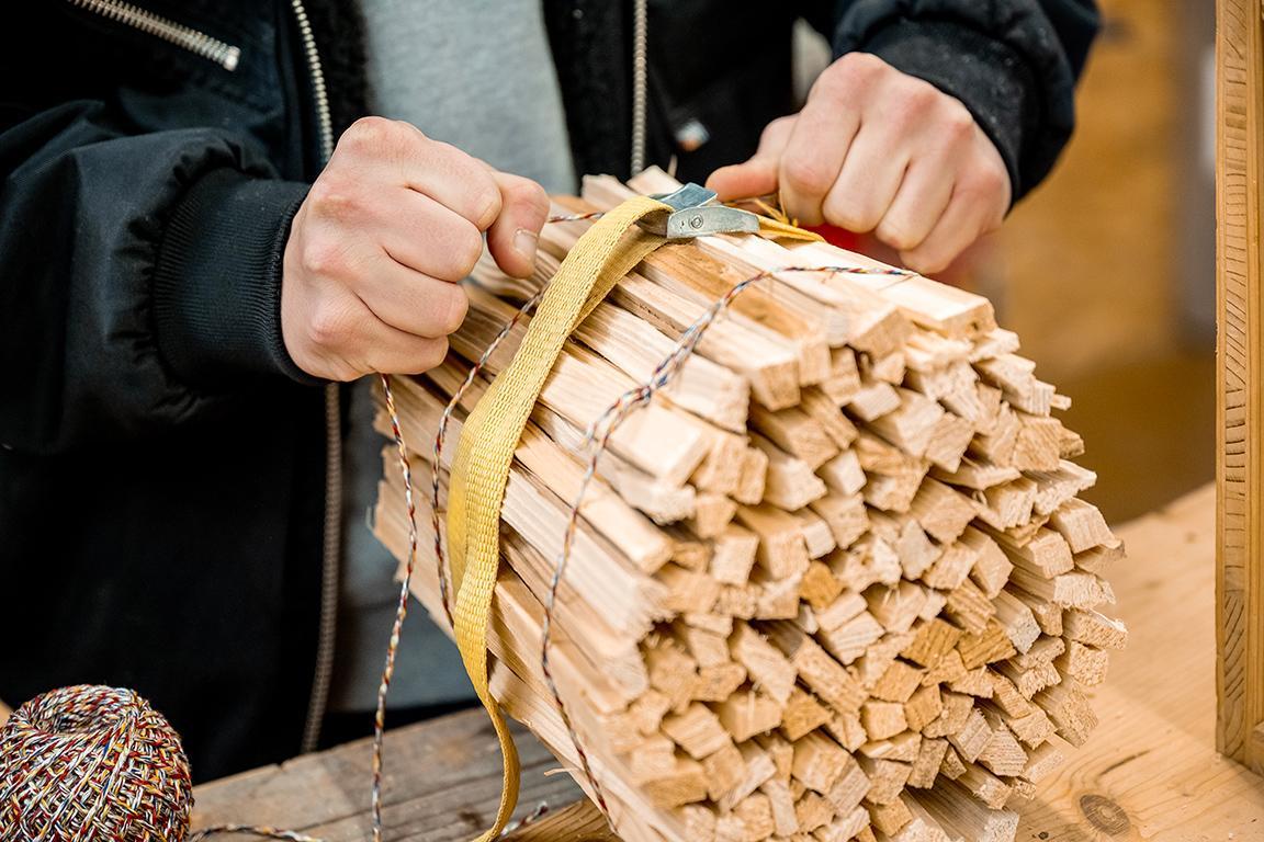 Ein Inhaftierter schnürt einen Haufen kleines Holz zum Anfeuern zusammen.