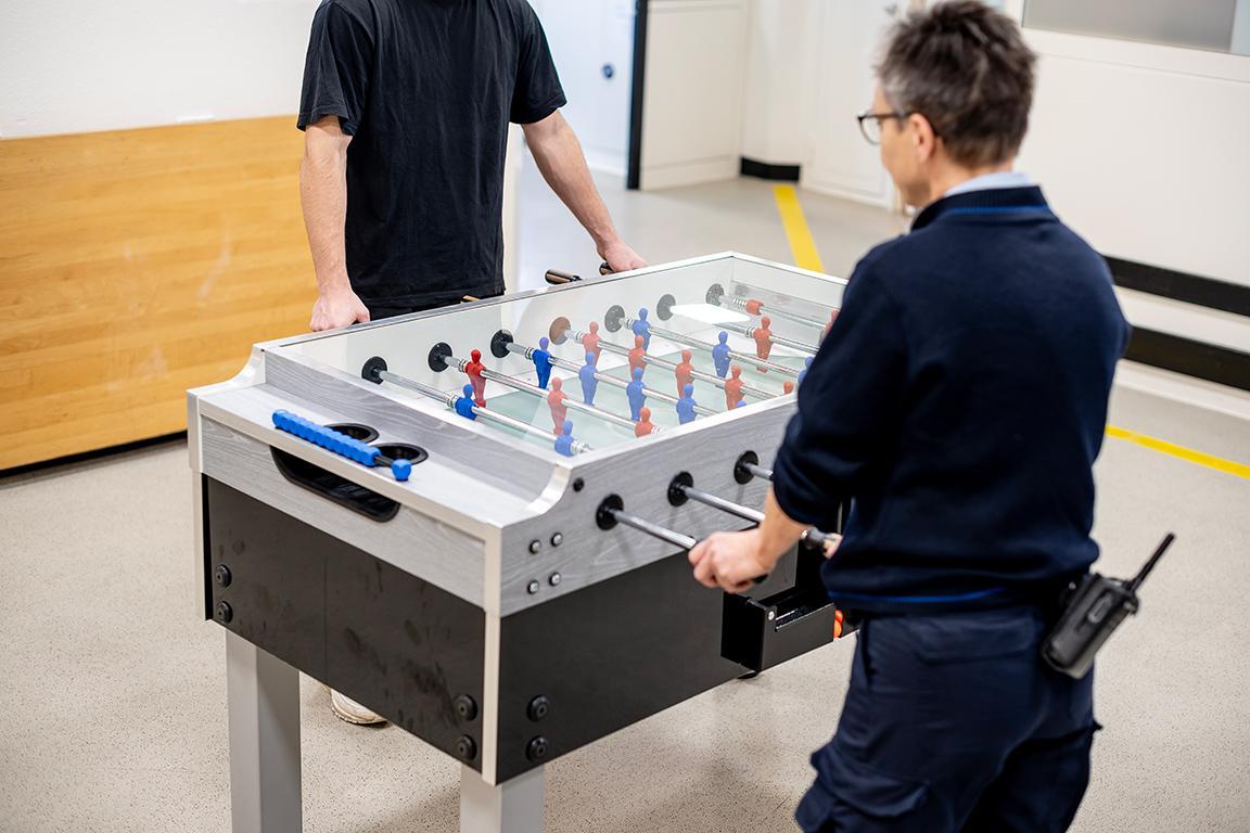 Eine Aufseherin/Betreuerin spielt Tischfussball mit einem Inhaftierten.