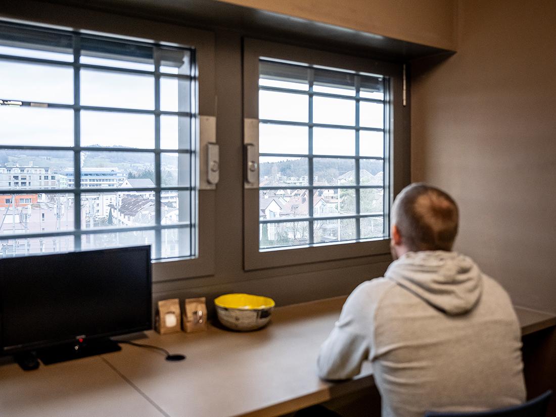 Eine Inhaftierte Person blickt aus einem vergitterten Fenster.