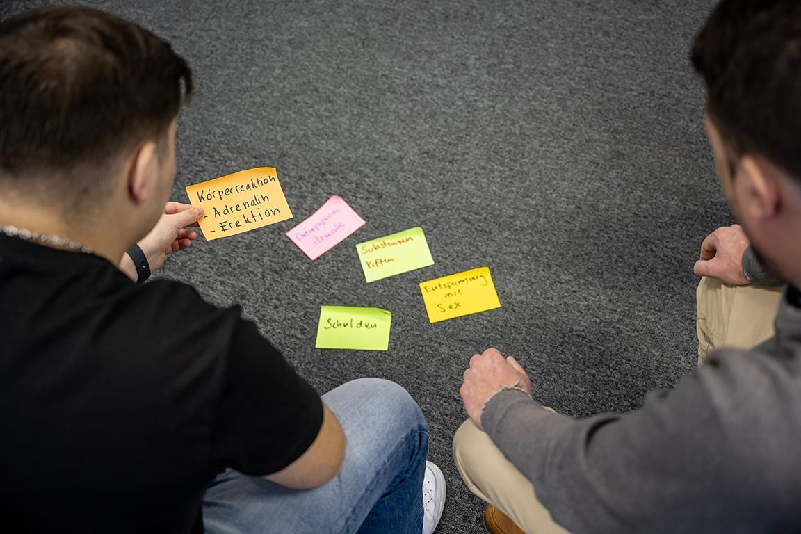Zwei Teilnehmer sind über am Boden liegende Post-it's gebeugt und unterhalten sich darüber.