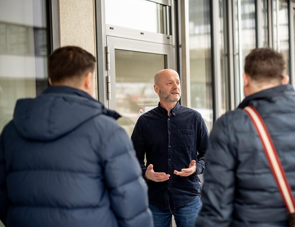 Der Kursleiter holt die Teilnehmer vor dem Gebäude ab.