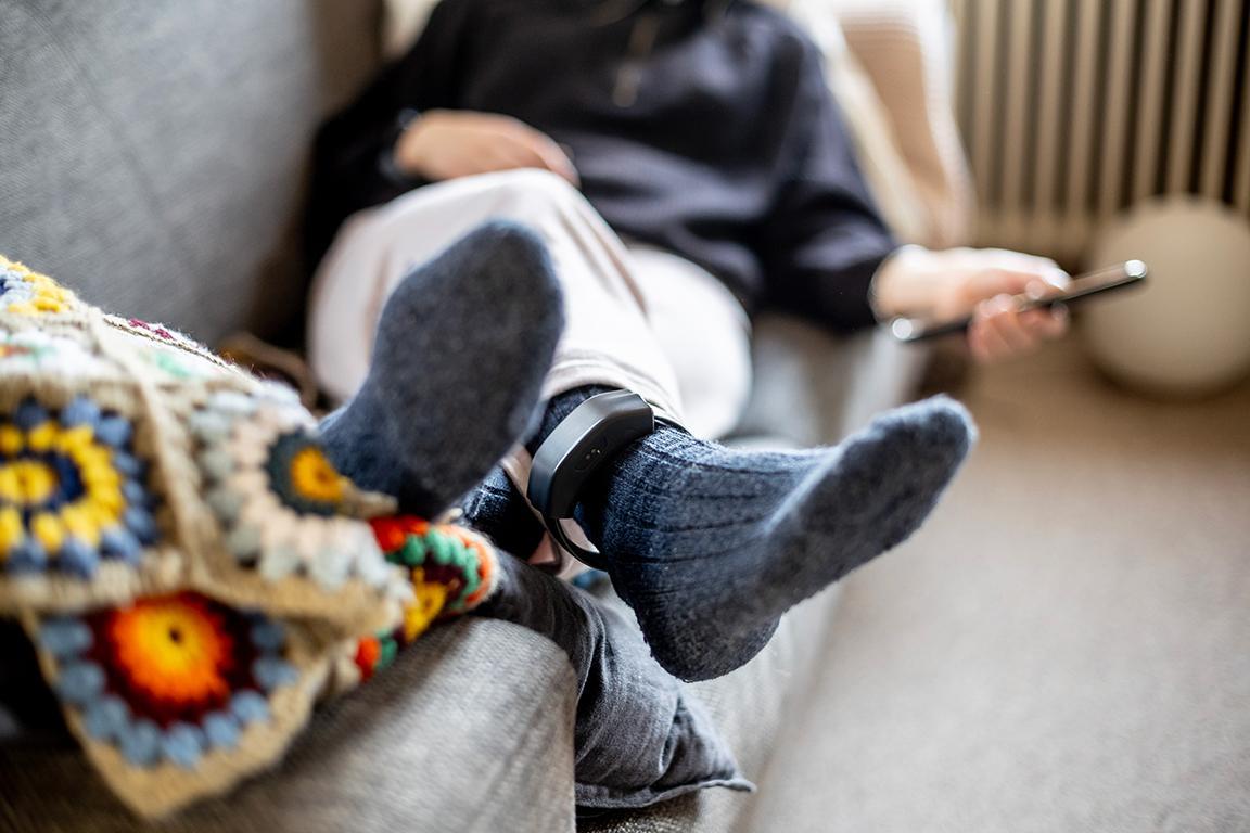 Eine Person liegt auf dem Sofa und hat eine Fussfessel um den Knöchel.