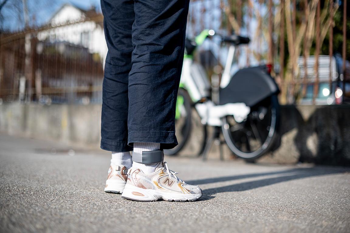 Eine Person, elektronische Fussfessel am rechten Fuss, steht für einem Velo.