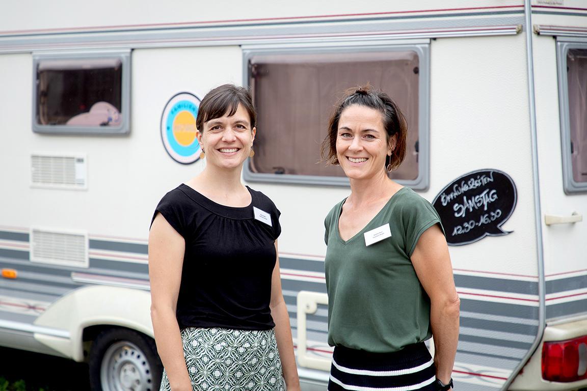 Zwei Frauen steht vor dem Wohnwagen und lächeln in die Kamera.