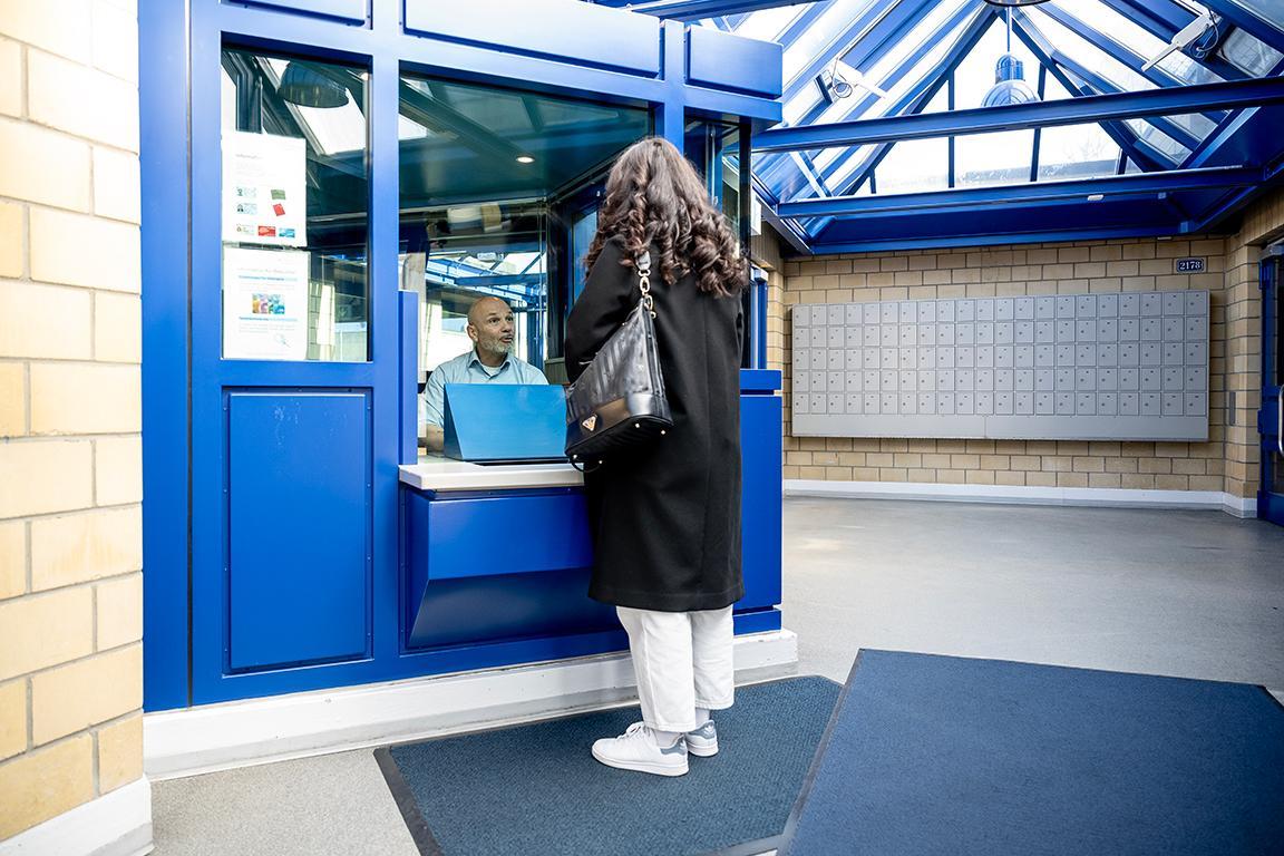 Eine Besucherin steht vor der Glasloge in der JVA Pöschwies und spricht mit einem Mitarbeitenden.