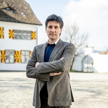 Der Direktor steht im Innenhof des MZU und schaut mit verschränkten Armen in die Kamera.