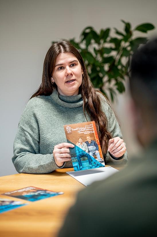 Mitarbeiterin hält im Gespräch mit einem Inhaftierten einen Flyer in der Hand.