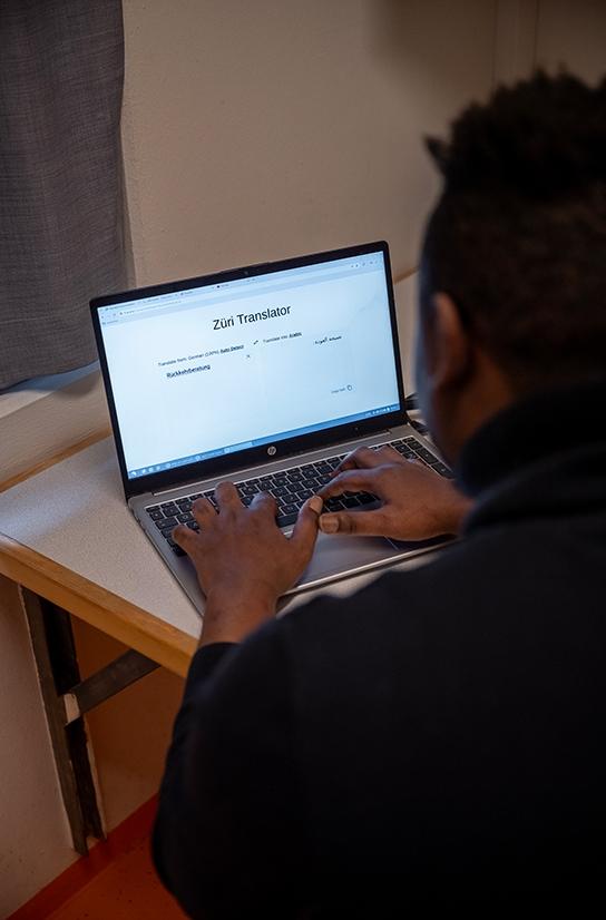 Ein Mann sitzt in seinem Haftraum vor einem Laptop und nutzt ein Übersetzungstool.