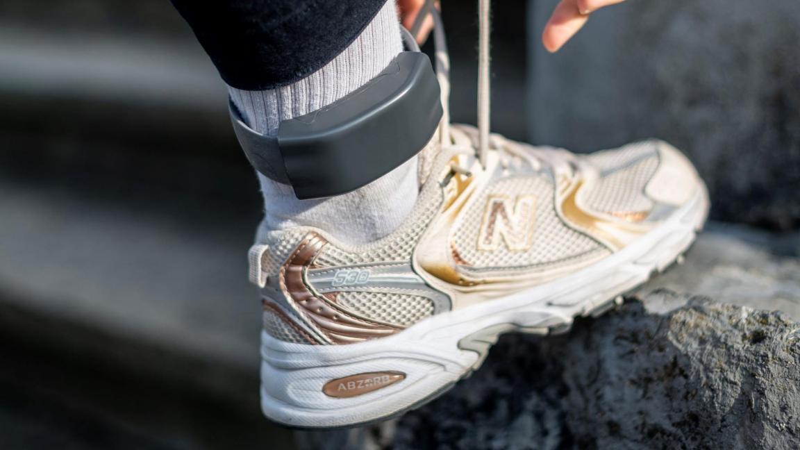 Person bindet sich die Schuhe, am Knöchel ist eine elektronische Fussfessel.