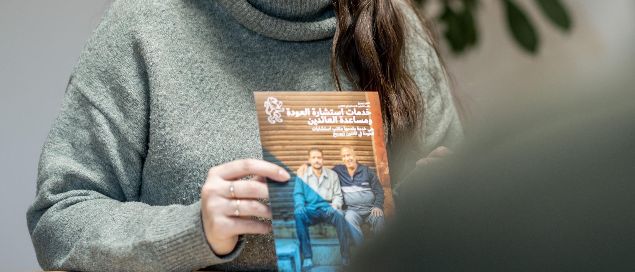 Frau hält einen Flyer zur Rückkehrberatung in der Hand.