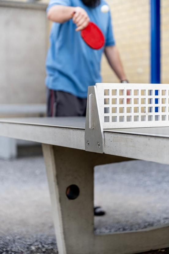 Ein Inhaftierter spielt mit einem roten Pingpongschläger auf dem Kiesplatz vor dem Betongebäude Pingpong.