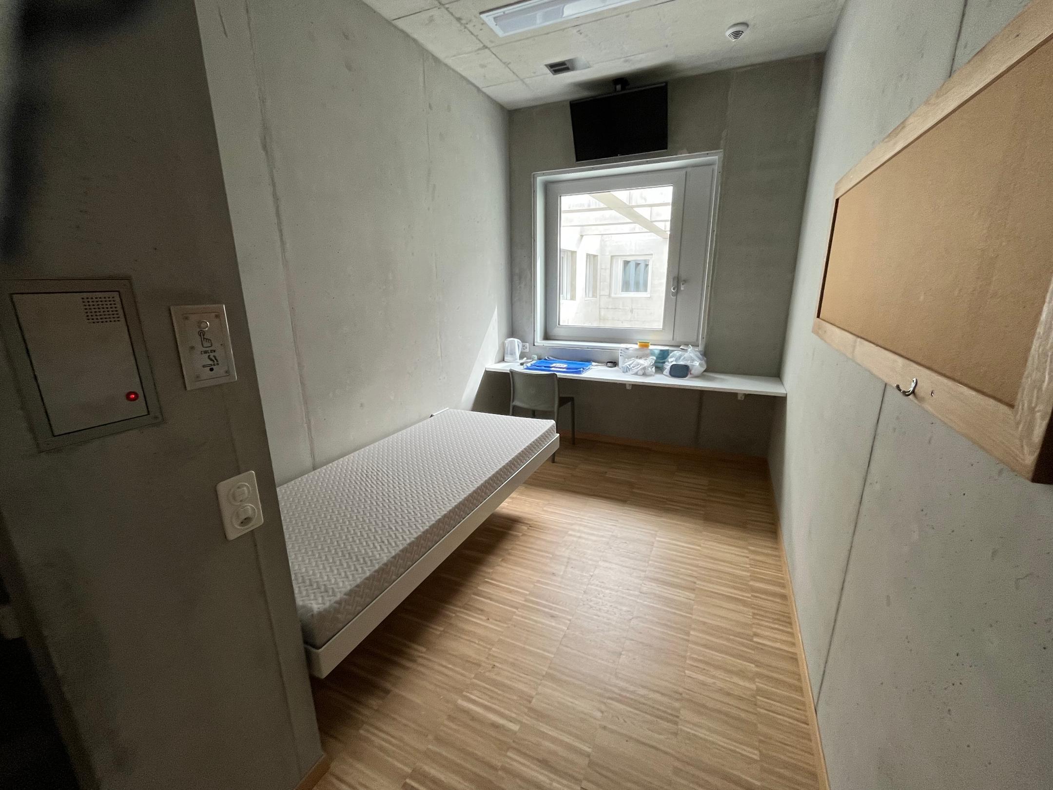 Eine Betonzelle mit einem Bett und einem Fenster