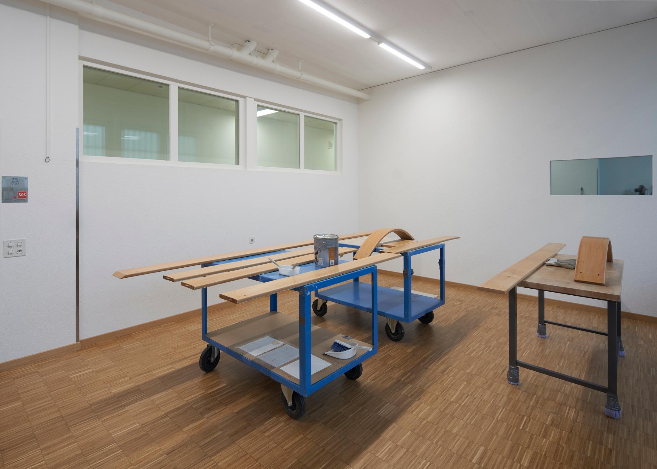 Auf dem Bild zu sehen sind Werkbänke, Holzstücke, ein Behälter mit Holzlasur und Lackierpinsel.